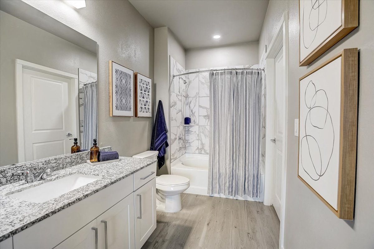 Bathroom with double-sink vanity, granite countertop, framed mirror, and tub-shower with tile surround.